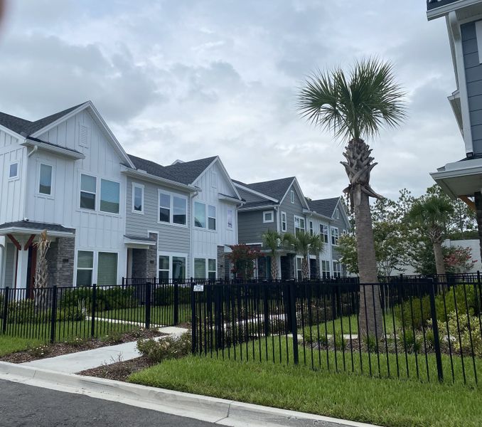 Modern townhomes with sleek siding, palm trees, and fenced lawns in Kettering at eTown by David Weekley Homes (Jacksonville, FL).