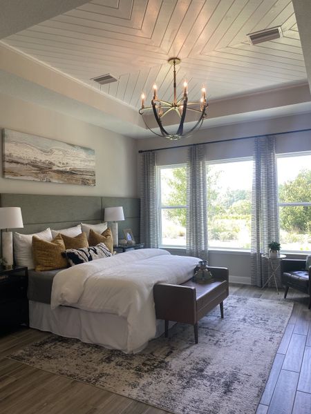 A cozy bedroom featuring a chic chandelier, stylish bedding, and expansive windows with scenic views.