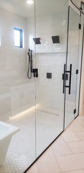 A modern bathroom featuring a sleek glass shower, hexagonal tiles, and chic black fixtures.