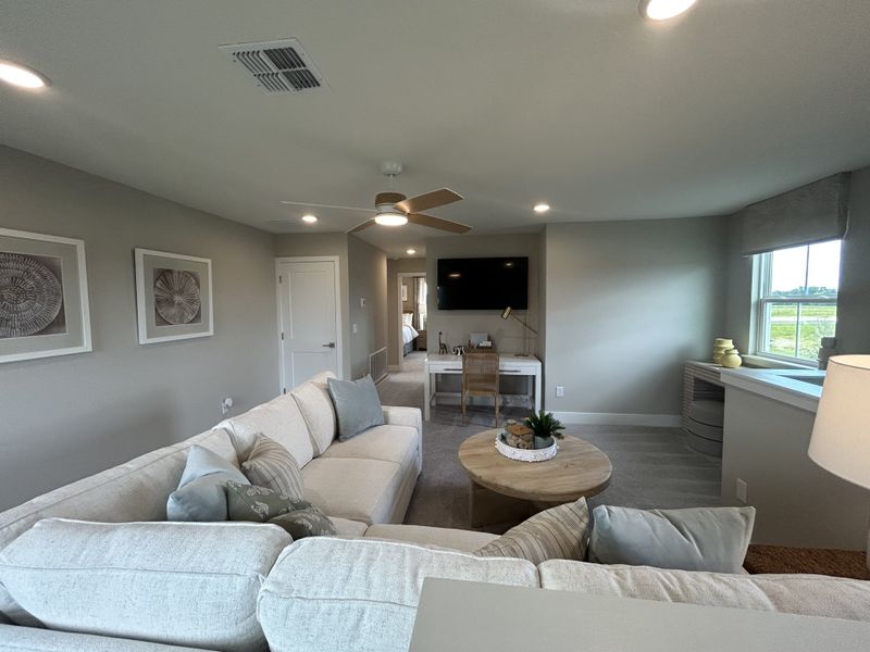 A cozy living room with a plush sectional, wooden accents, and a desk area, enhanced by soft lighting and neutral hues.