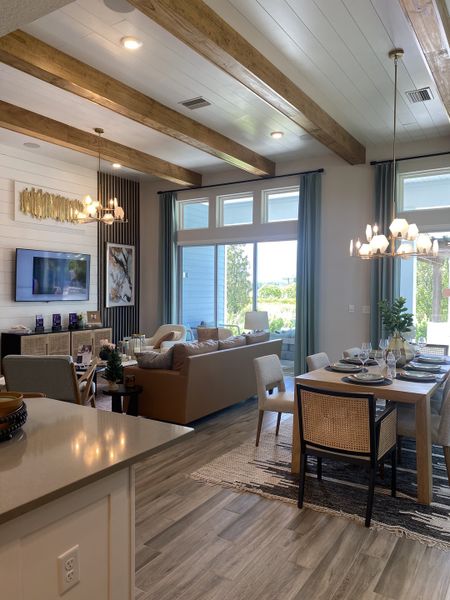 A modern living-dining area with wood beams, elegant lighting, and large windows, creating a bright, inviting ambiance.