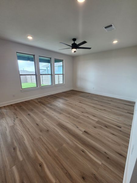 A spacious room with natural wood flooring, large windows, and a sleek ceiling fan, offering ample light and modern style.