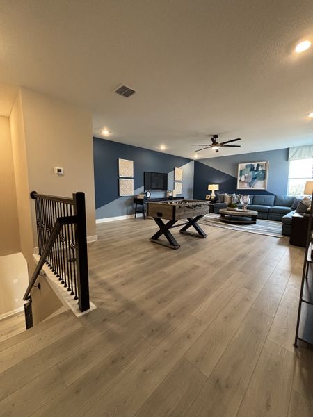 A spacious loft area with contemporary furnishings, wood flooring, and an accent wall, perfect for relaxation or entertainment in Crossroads at Kelly Park by Dream Finders Homes (Apopka, FL).