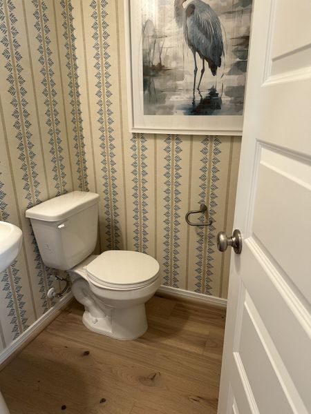 A cozy bathroom with patterned wallpaper, wood flooring, and elegant artwork featuring a heron.