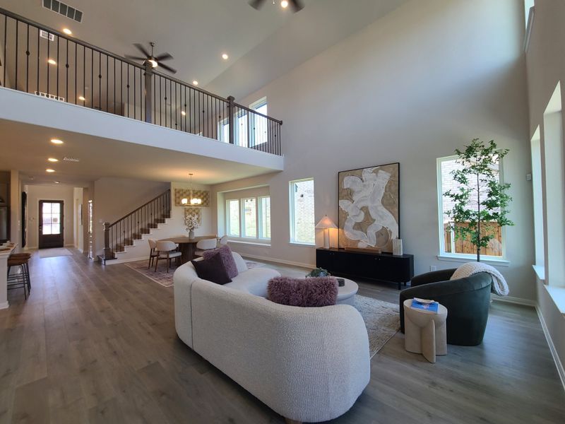 An elegant living space featuring high ceilings, modern railing, a cozy seating area, and abundant natural light.
