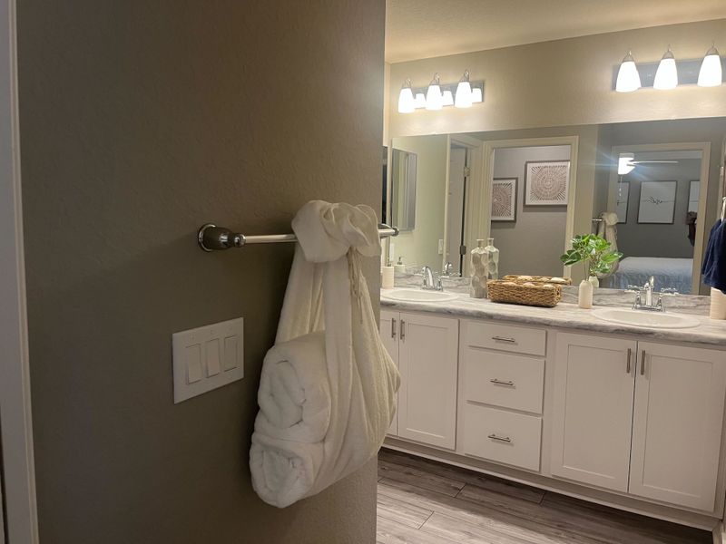 A modern bathroom with dual sinks, soft lighting, white cabinetry, and decorative accents for a cozy atmosphere.