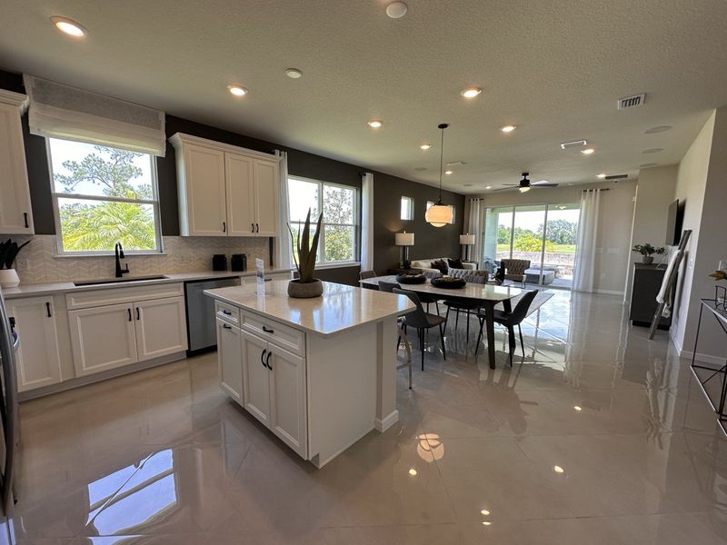 Spacious open-concept kitchen and dining area with sleek cabinetry, modern lighting, and large windows overlooking greenery.