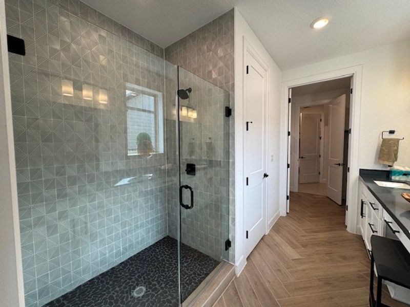 A modern bathroom with a geometric-tiled shower, sleek black fixtures, and warm wood flooring.