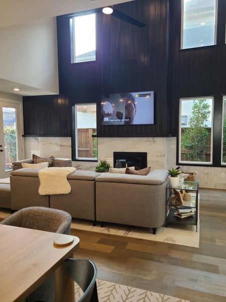 A modern living room with high ceilings, a sleek fireplace, elegant wood paneling, and cozy sectional seating.