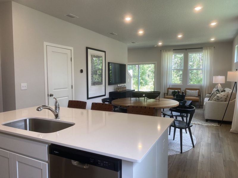 A modern open-concept living area with a sleek kitchen, wood flooring, and ample natural light through large windows. A modern open-concept living area with a sleek kitchen, wood flooring, and ample natural light through large windows.