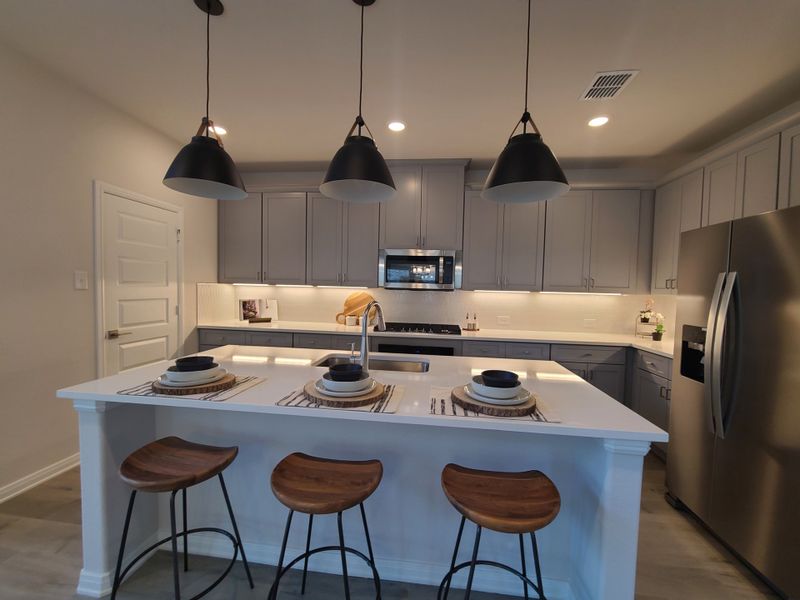 A modern kitchen with gray cabinets, a large island, pendant lighting, and stylish wooden stools.