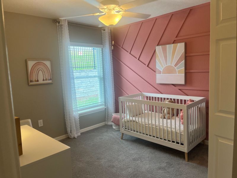 A cozy nursery with a modern crib, pink accent wall, and soft carpet, creating a warm and inviting atmosphere.