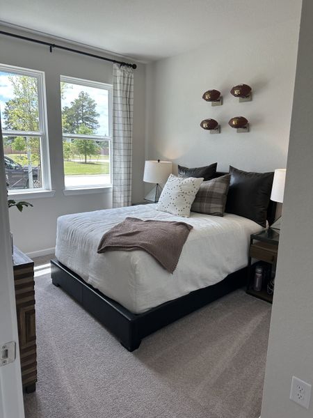 A cozy bedroom with neutral tones, twin windows, and decor featuring football-themed wall accents and plush bedding. A cozy bedroom with neutral tones, twin windows, and decor featuring football-themed wall accents and plush bedding.