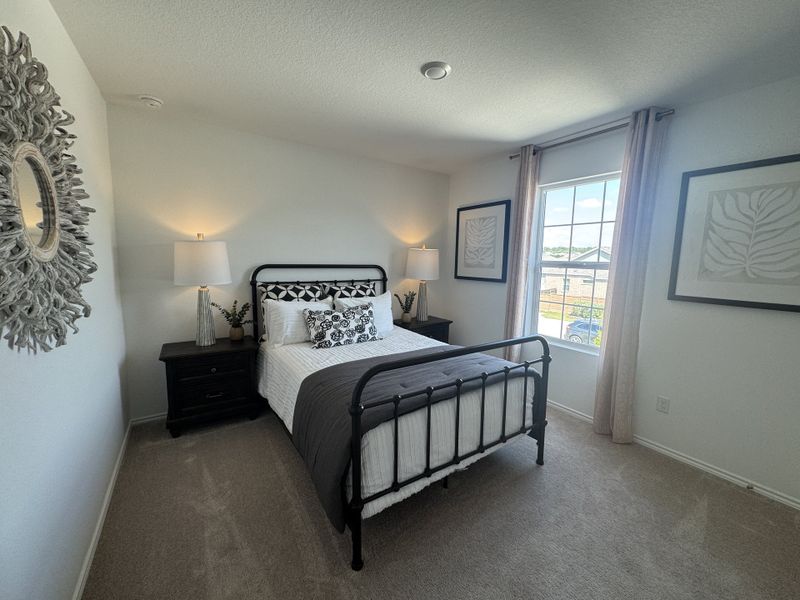 A cozy bedroom with a black metal bed, elegant decor, and ample natural light from a large window.