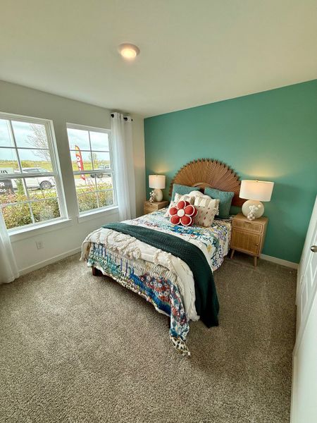 A cozy bedroom with a teal accent wall, patterned bedding, and natural light pouring through large windows.
