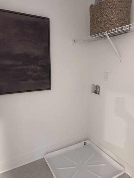 A minimalist laundry room with a wash station, wire shelf, and abstract artwork.