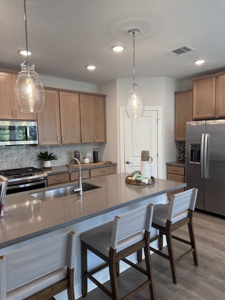 A modern kitchen with a sleek island, wooden cabinets, pendant lighting, and stainless steel appliances.
