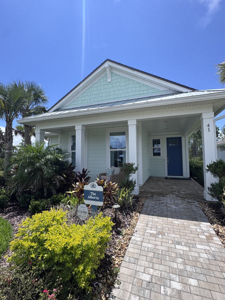 A charming mint-green home with a cozy porch and lush landscaping in Seabrook Village at Seabrook by Providence Homes (Nocatee, FL).