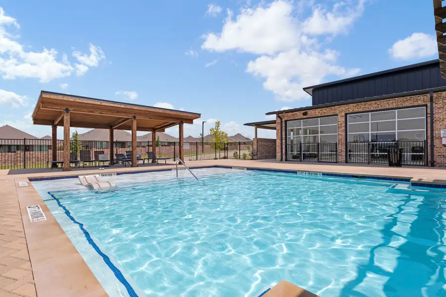 Community pool with wood pergola, brick clubhouse, and black iron fence surrounding the deck area