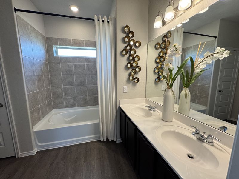 A modern bathroom with a tiled bathtub, dual sinks on a sleek vanity, and elegant decorative accents.