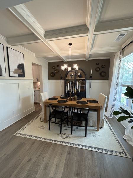 A cozy dining room featuring a wooden table, elegant chandelier, and coffered ceiling with classic decor accents.