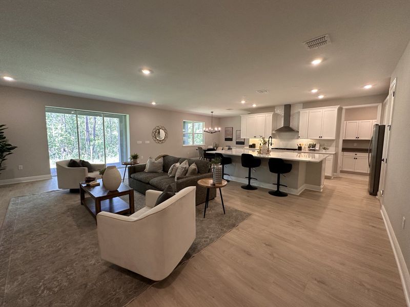An open-concept living room with cozy seating, modern kitchen, and sleek flooring, complemented by ample natural light.