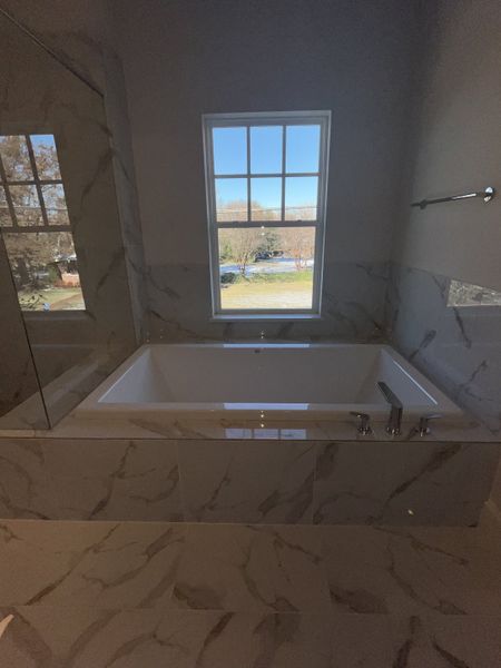 A luxurious bathroom with a marble surround bathtub and a window view, offering elegance and relaxation. A luxurious bathroom with a marble surround bathtub and a window view, offering elegance and relaxation.