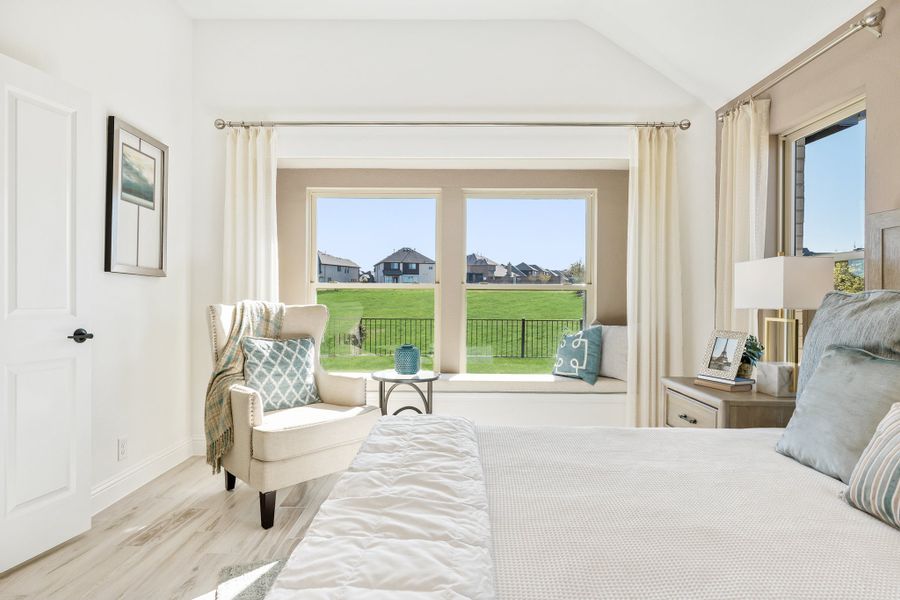 Bright bedroom with vaulted ceiling, window seat, and large windows overlooking a green yard