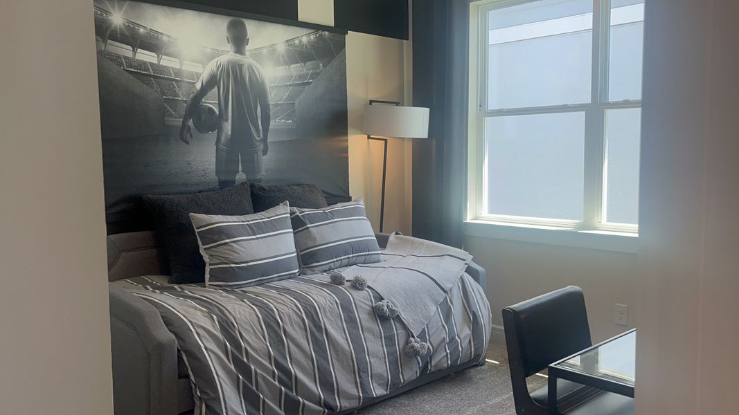 A cozy bedroom with a striped bedspread, soccer-themed artwork, and sleek furnishings adds a modern touch.