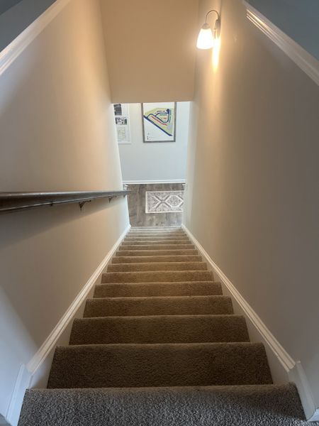 A cozy carpeted staircase with a wall sconce lighting, leading to a warmly lit space and decorative artwork. A cozy carpeted staircase with a wall sconce lighting, leading to a warmly lit space and decorative artwork.
