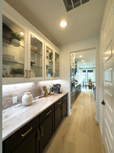 A modern hallway with sleek cabinetry, glass shelves, and elegant lighting leading to an open, bright kitchen and dining area. A modern hallway with sleek cabinetry, glass shelves, and elegant lighting leading to an open, bright kitchen and dining area.