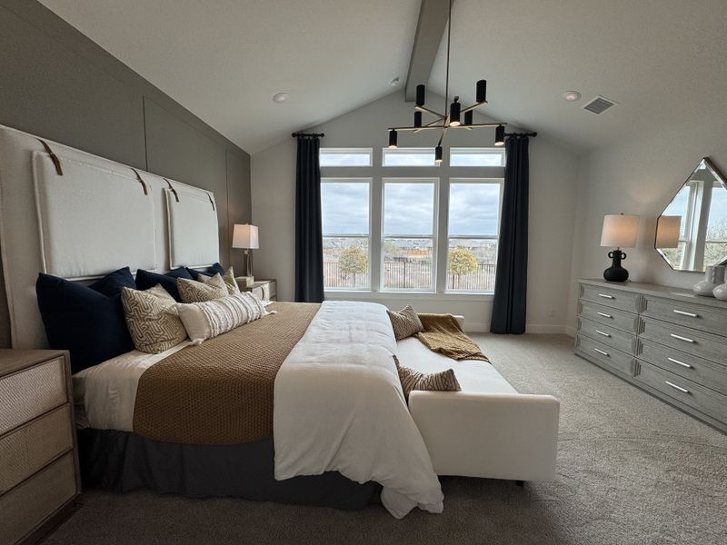A spacious bedroom features a plush bed, elegant chandelier, large windows, and stylish decor in neutral tones.