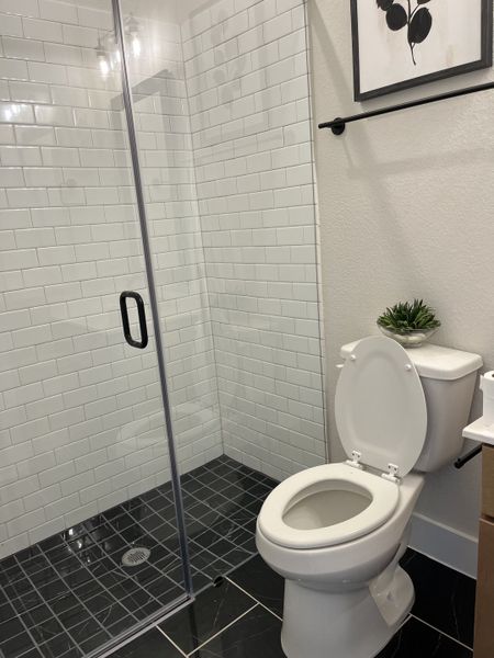 A sleek bathroom featuring a glass shower, subway tiles, and black floor tiles with modern accents.