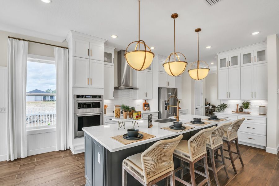 Kitchen with white cabinets, large island with four bar stools, and three gold pendant lights overhead. Kitchen with white cabinets, large island with four bar stools, and three gold pendant lights overhead.