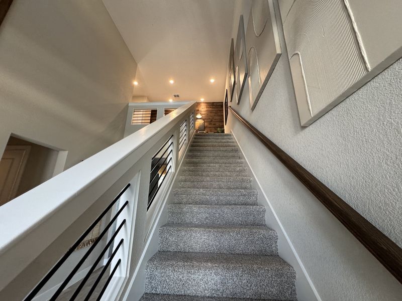 A modern staircase with sleek railing and textured art on soft-colored walls, leading to a bright landing area.