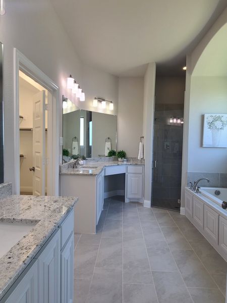 Elegant bathroom featuring granite countertops, a spacious shower, dual vanities, and soft, ambient lighting.