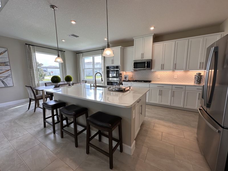 A spacious kitchen with sleek white cabinetry, stainless steel appliances, and a large island with seating in a bright open layout.