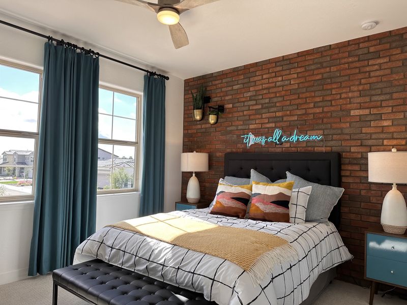 A cozy bedroom featuring a brick accent wall, bold pillows, and modern decor with teal curtains and warm lighting.