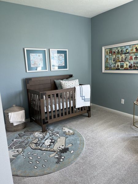Charming nursery with a wooden crib, whimsical round rug, soft gray carpet, and playful art on blue walls.