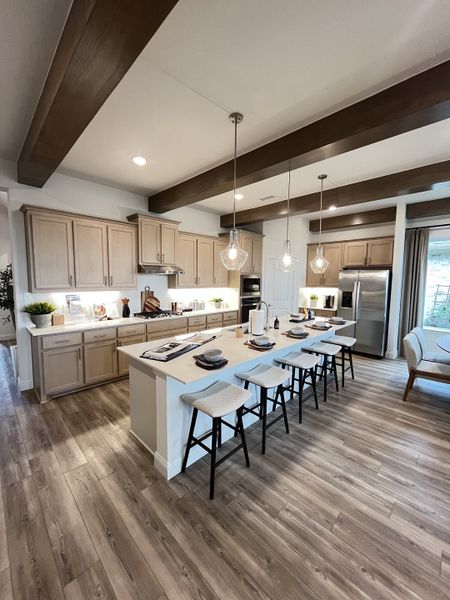 A modern kitchen featuring wood beams, sleek cabinetry, and an island with stylish seating and pendant lighting.