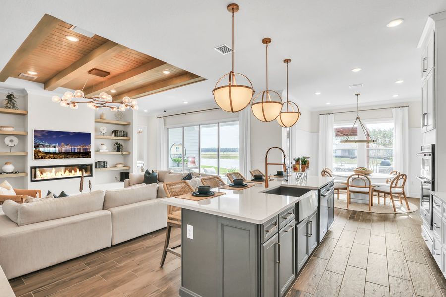 Open-concept kitchen with gray island, pendant lights, and living area with fireplace and built-in shelves