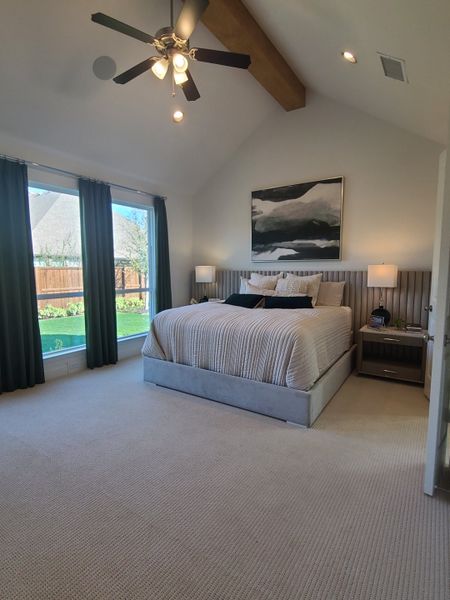 A spacious bedroom with vaulted ceilings, plush carpeting, a cozy bed, and large windows draped with elegant curtains.