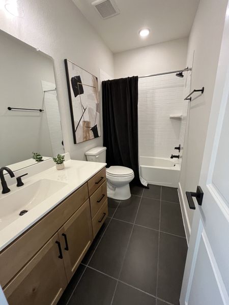 A modern bathroom featuring a sleek vanity, abstract art, and a chic black-tiled floor.