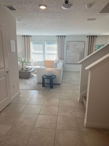 An elegant living area features a cozy white sectional, abstract art, and natural light streaming through large windows.