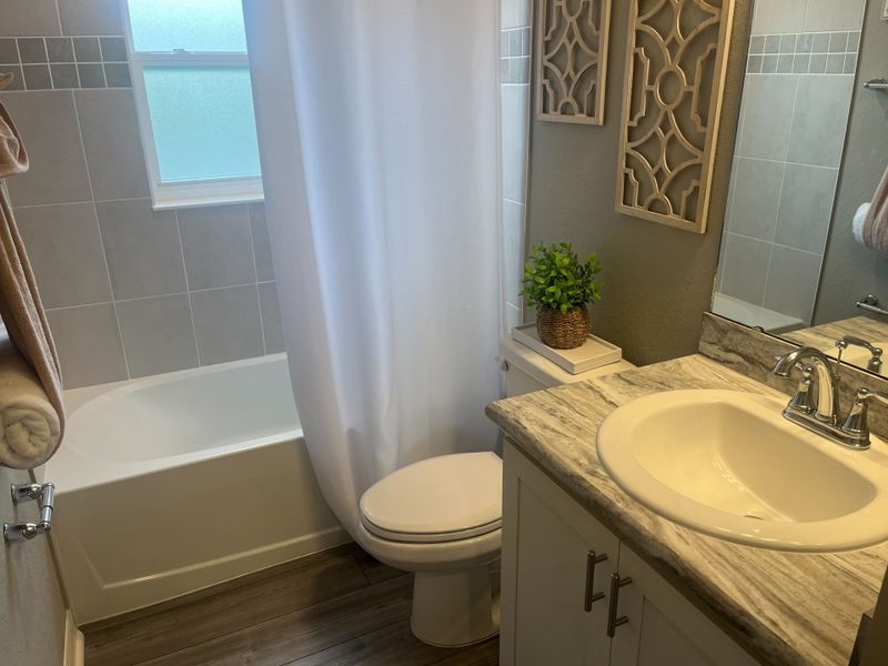 A cozy bathroom featuring a sleek granite countertop, white sink, gray tiled walls, and elegant decor accents.