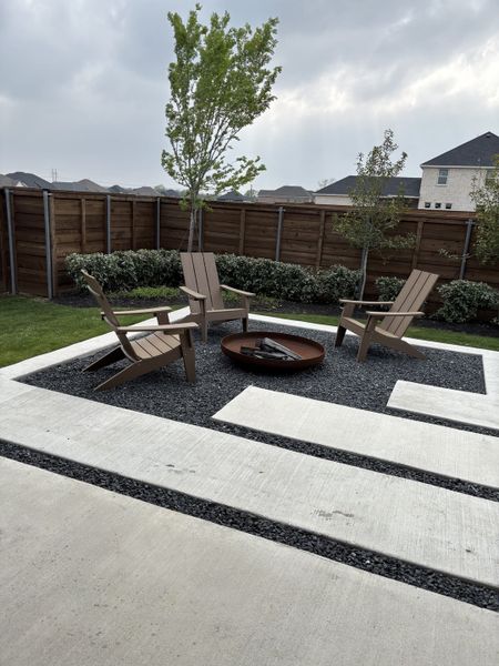 A modern outdoor area with a fire pit, Adirondack chairs, and sleek paving, perfect for relaxing evenings.