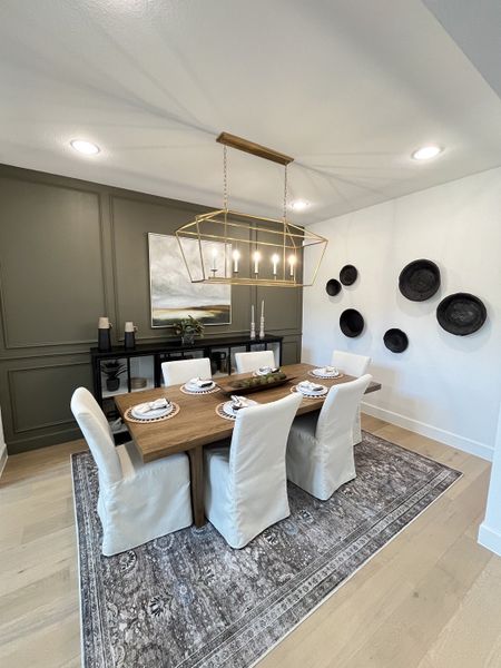 A chic dining room with a wooden table, white slipcovered chairs, gold pendant light, and decorative accents.