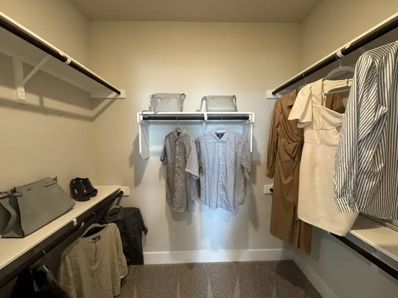 A spacious walk-in closet with ample shelving, hanging space, and neutral carpet flooring for organized storage.