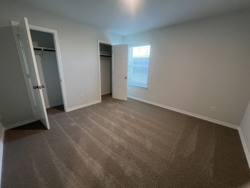A cozy bedroom with fresh carpet, soft gray walls, ample closet space, and bright natural lighting.