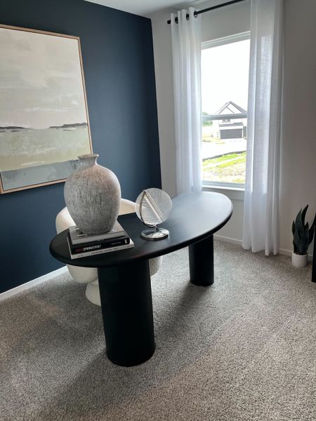 A contemporary office with a sleek black desk, elegant decor, and a large window with sheer curtains.